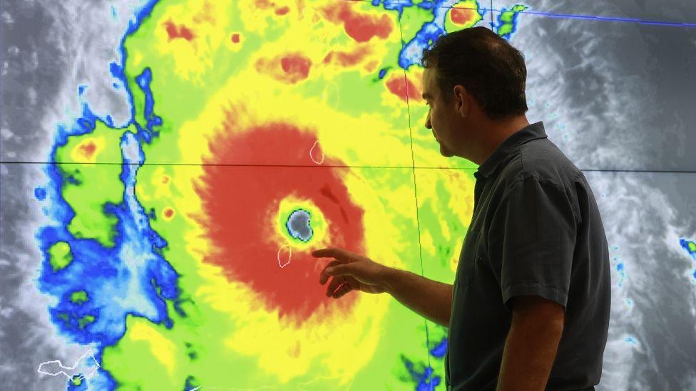 A man inspects a coloured image of a hurricane on a giant screen at the National Hurricane Center run by the NOAA in the United States 