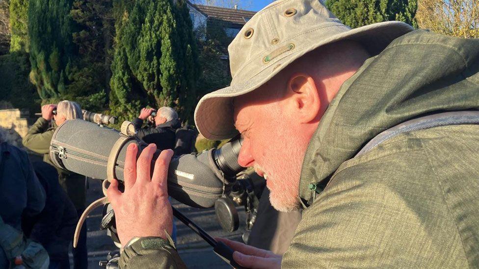 Paul, dressed in green, peers through a long lens to see the Scarlet Tanager.