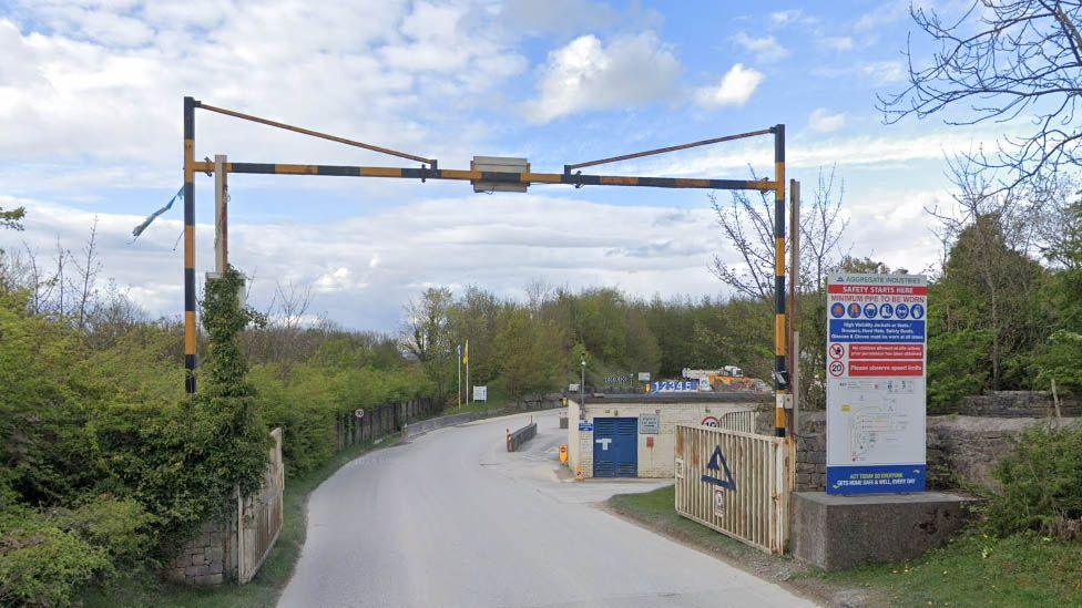 The entrance to Back Lane quarry showing a sign indicating safety gear must be worn to the right of a barrier over a road