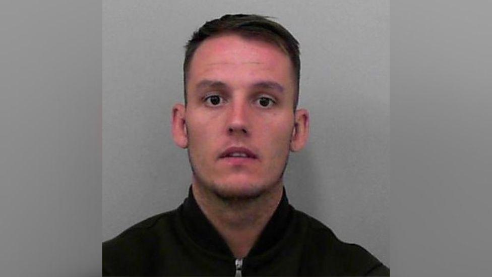 A police custody photo of Joe Hatherall. He has short dark-brown hair and is wearing a black zip-up jacket.