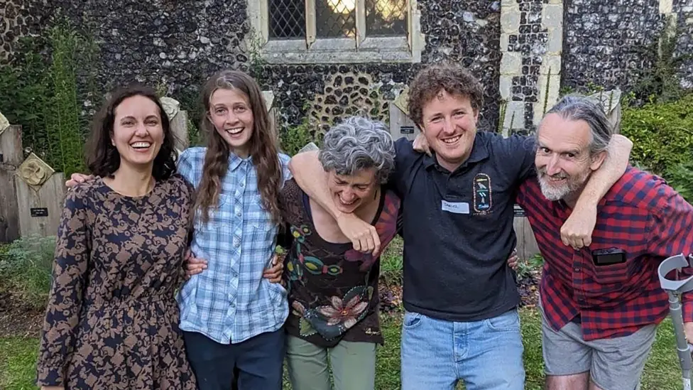 Climate protesters stand in a row whilst smiling and laughing, in a church graveyard