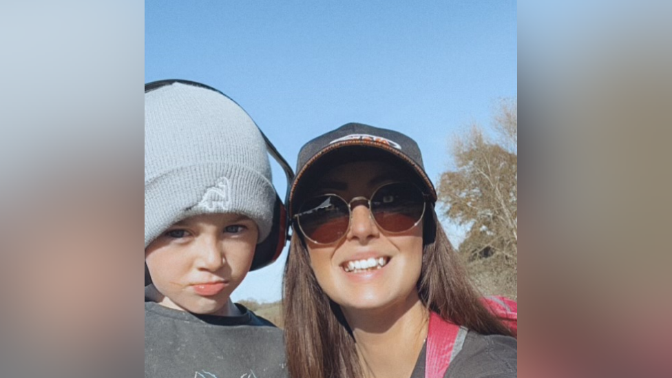 A woman in a baseball cap with a young boy wearing a woolly hat.