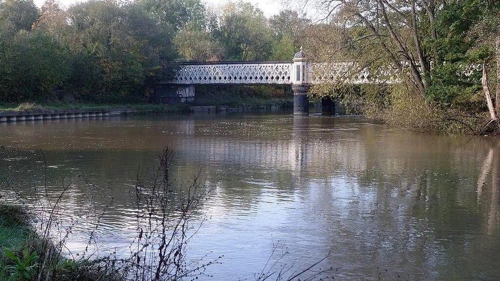 An iron bridge dating back to the 19th Century spans the Thames, with criss-crossing metal bars forming its sides. 