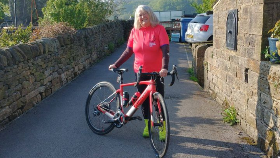 Liz Barrett standing outside, next to a pink bicycle 