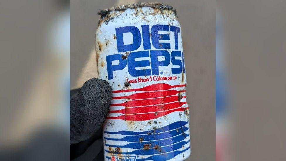 Close-up of an old Diet Pepsi can being held up. It has rusty spots all over it with "Diet Pepsi" written in blue and several red and blue lines below. It also says "less than one calorie per can" on the can.