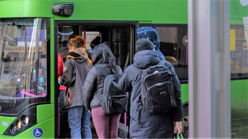 three people in dark clothes getting on a green bus