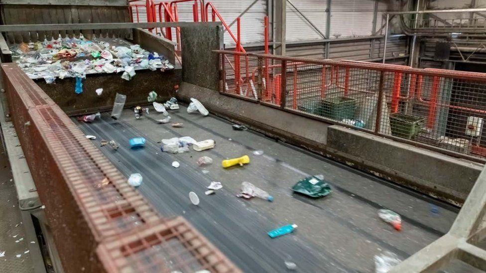 Conveyor belt with recycling rubbish on the move and a large pile ready to drop onto the belt to the left