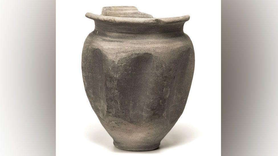 A nearly intact Roman beer beaker with a narrow base and a wider middle, narrowing to a slightly smaller rim