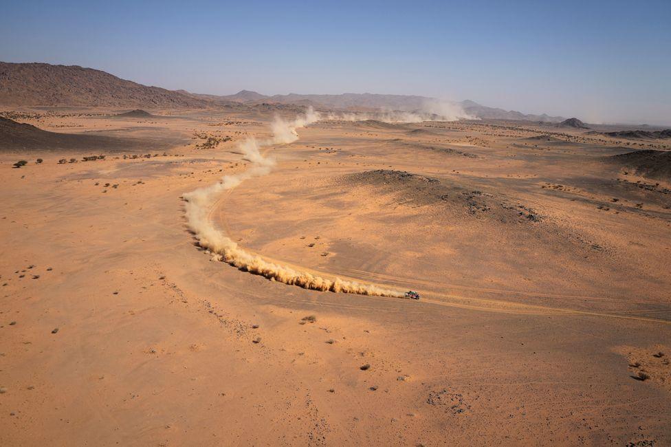 A car is followed by a dust trail in the Saudi desert, as it takes part in the Dakar Rally.