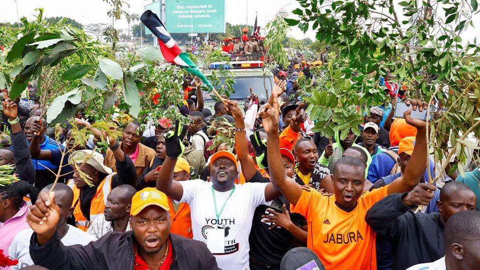 Crowds surround the cortege taking Raila Odinga's coffin through Nairobi - many holding the branches of trees - 16 October 2025.