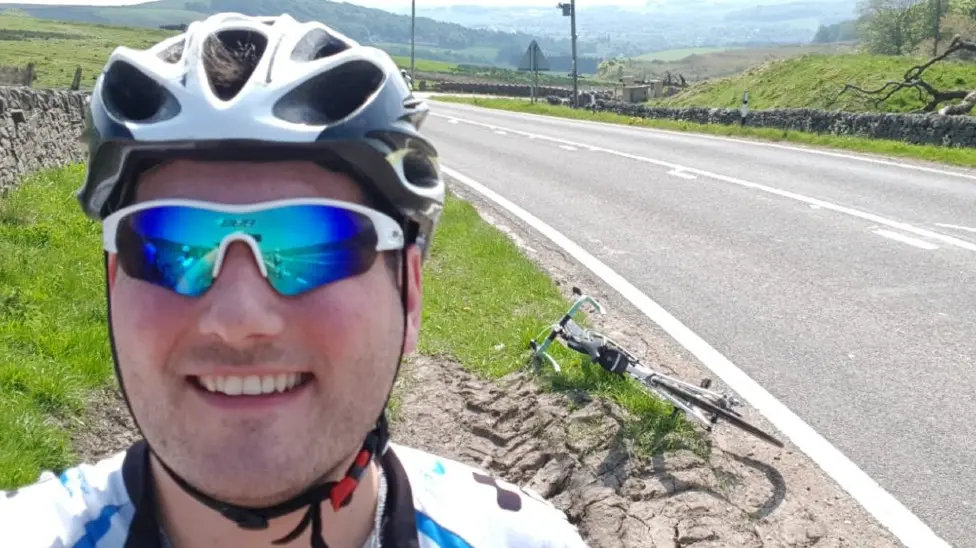 Sam Perkins pictured with a bike helmet and sunglasses next to an empty road