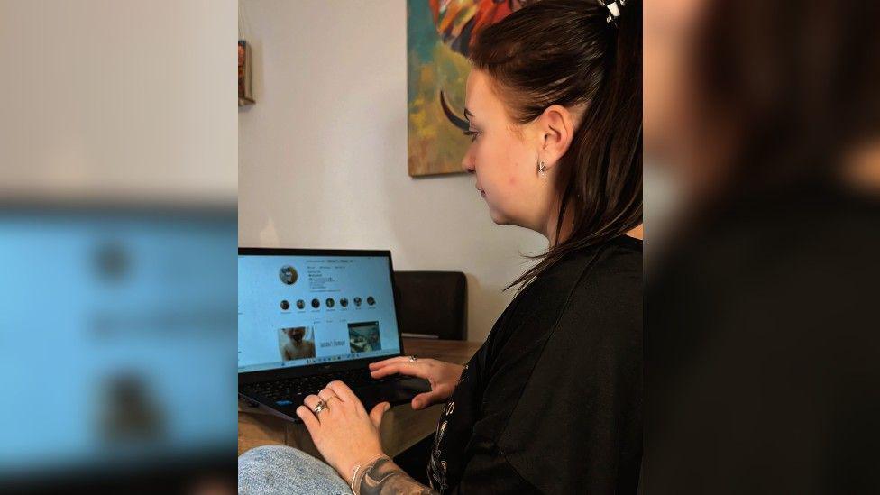 Sophie sitting at a computer with her Instagram account showing. 