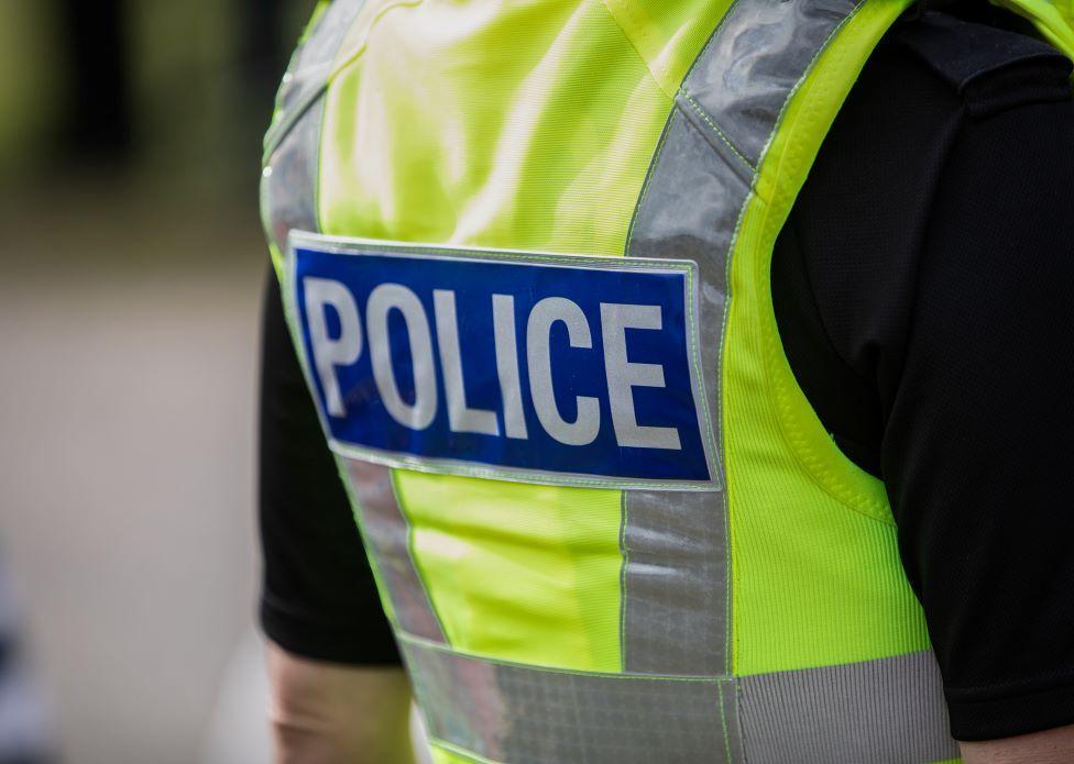 Police officer wearing a high vis jacket that says "police" on the back