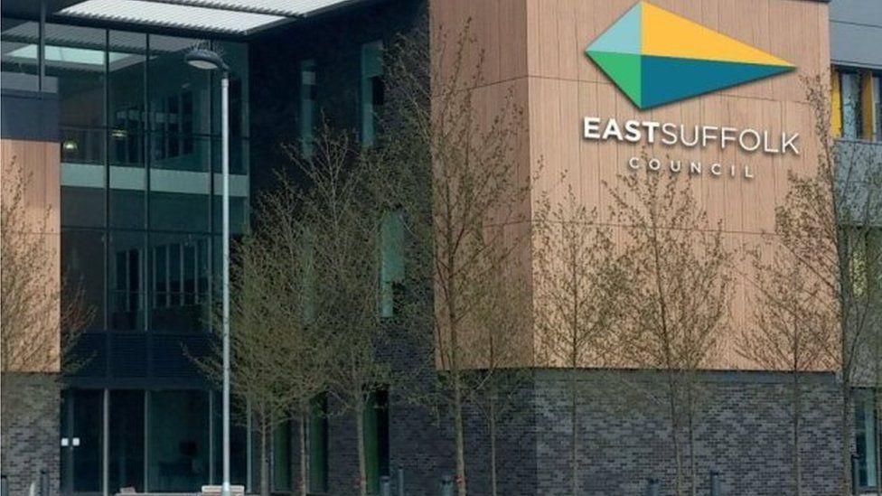 A view of the exterior of East Suffolk Council's headquarters. The council's name and diamond-shaped logo is on part of the building, which is modern and has three storeys.