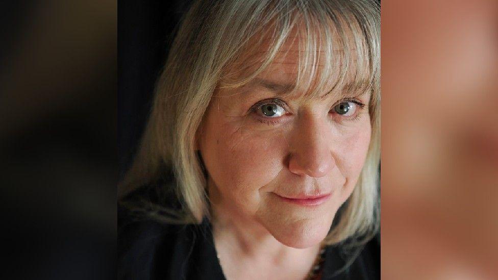 A headshot of Tiffany, a woman in her 50s with greying blonde hair
