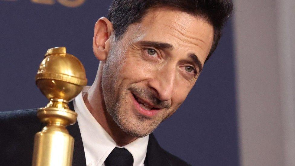 Adrien Brody holding up his the award for best actor in a drama, for The Brutalist