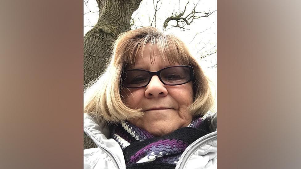 A selfie of an older woman wearing a purple stripey scarf and glasses. 