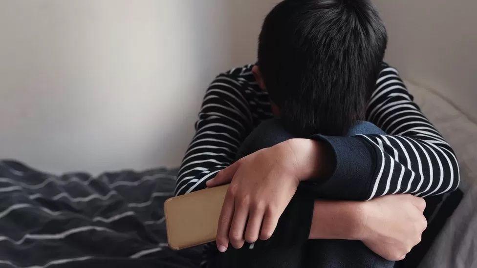 A child with their head on their knees, covering their face. 