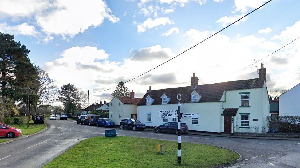 View of the village green in Bassingham with a black and white fingerpost direction sign in the foreground and a white cottage in the background.