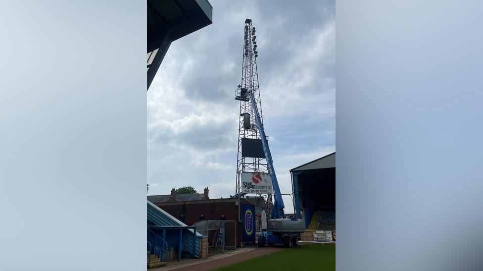 Huge cherry-picker type crane preparing to dismantle the floodlight pylon