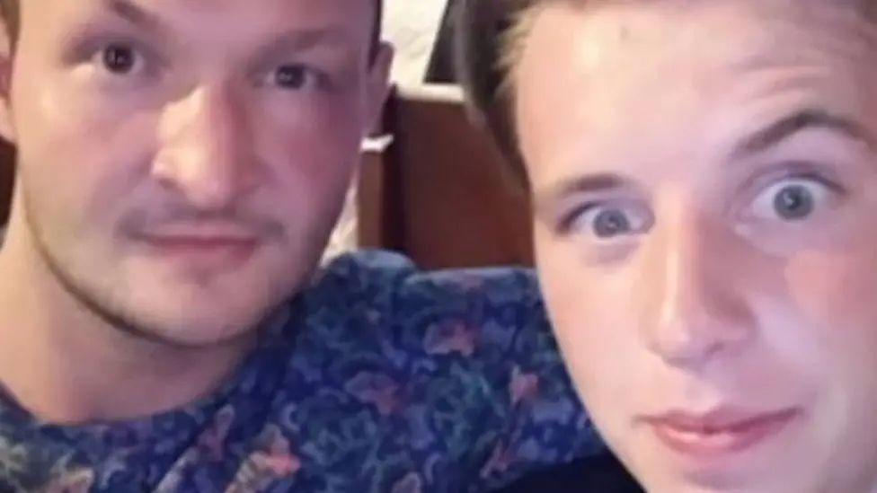George Low, in a patterned blue top, has his arm around his friend Ben Barker as they both look at the camera lens
