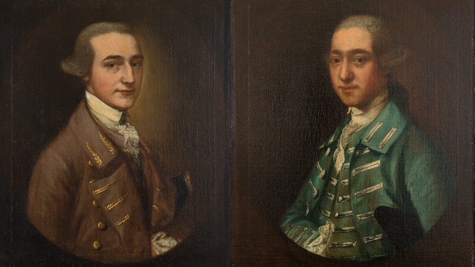 William Tugwell and Thomas Tugwell. William wears a brown regency coat and has a cravat, while Thomas has a green overcoat on. Both have wigs and were painted on a brown background.