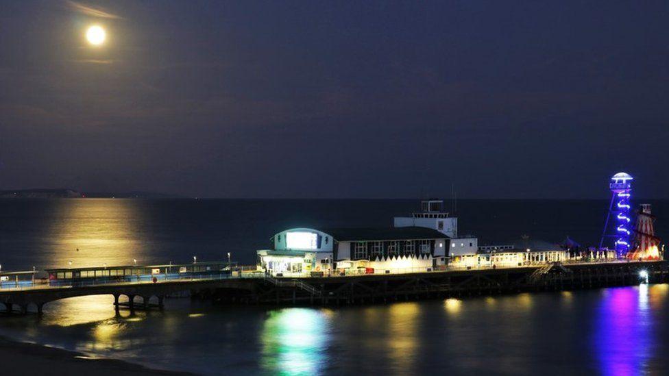 The pier lit up with the bright moon high in the sky reflecting in the sea