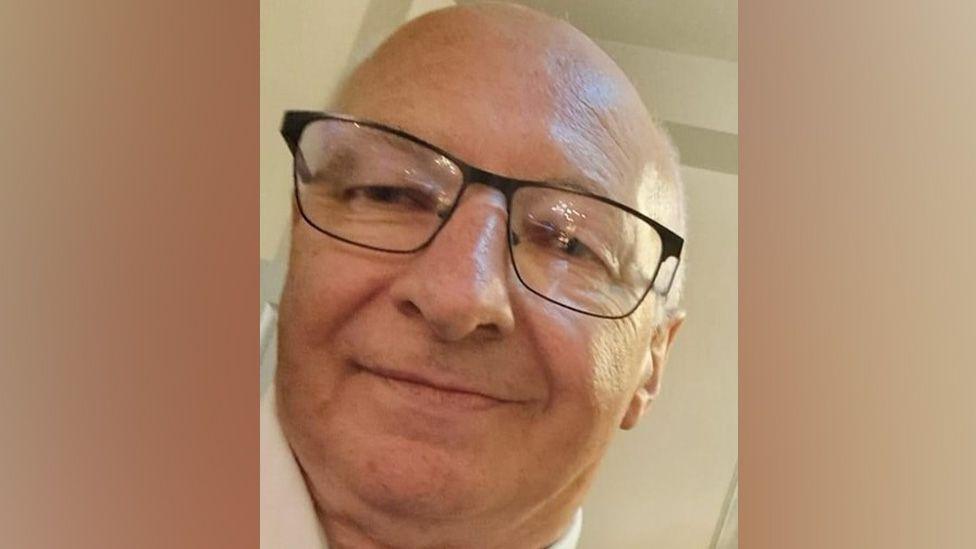 Photograph of Bernard Payne. He is smiling, bald and is wearing dark-rimmed glasses.