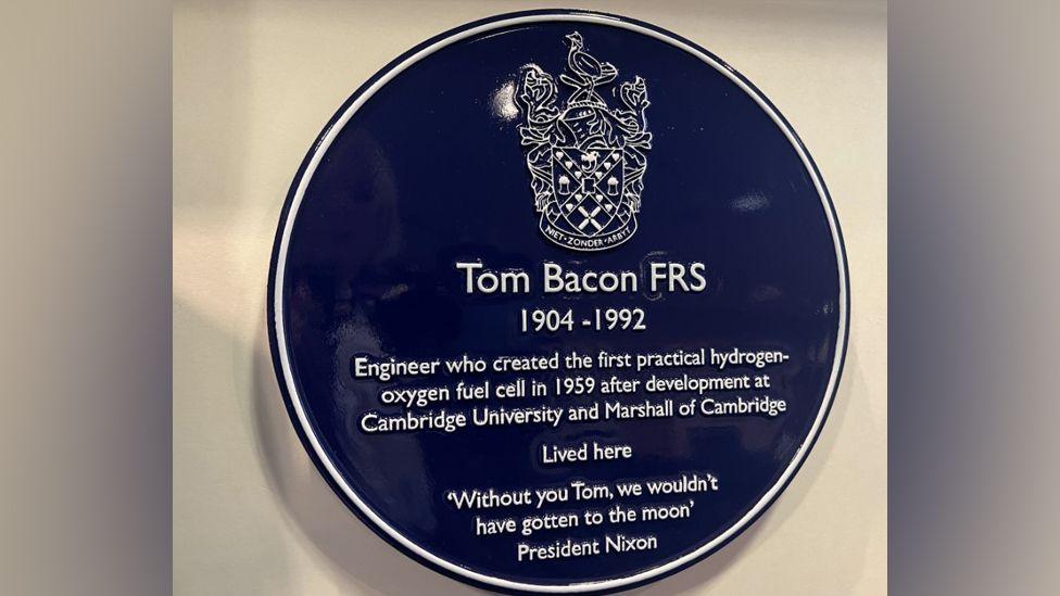 A blue plaque on a cream wall. It recognises the achievements made by scientist Tom Bacon and includes a quote from President Nixon