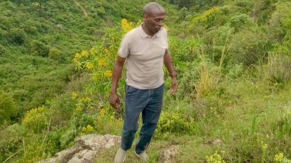 A man standing among green plants