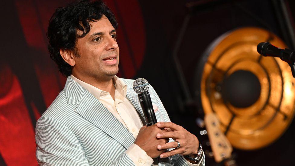 M. Night Shyamalan wearing a white shirt and blue pin-striped blazer