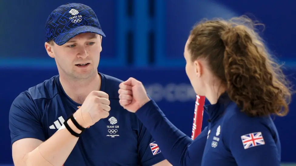 Bruce Mouat and Jen Dodds bump fists as they wear blue team outfits
