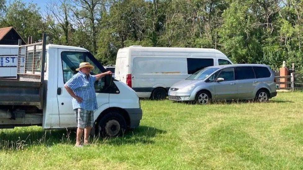 A man standing by a van in a field