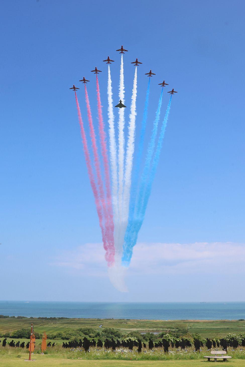 The Red Arrows with a Eurofighter EF-200 Typhoon accompanying them flypast the UK Ministry of Defence and the Royal British Legion’s commemorative event at the British Normandy Memorial to mark the 80th anniversary of D-Day on June 06, 2024 in Ver-Sur-Mer, France. 