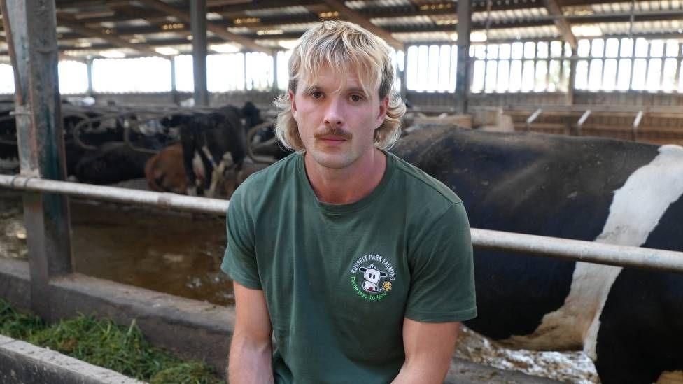 A man with long blonde hair and a moustache wearing a green t shirt