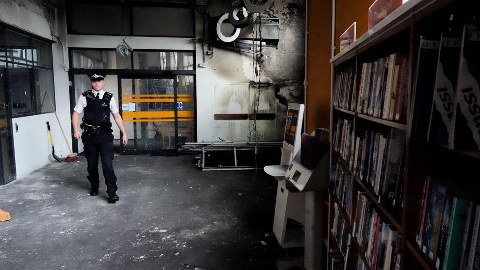 A police officer walks inside the Spellow Library after it was targeted and damaged by rioters