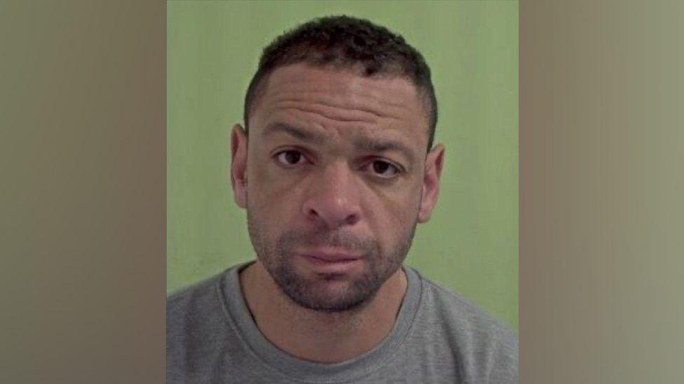 A mugshot of James Doherty, in his early forties, wearing a grey crew-neck shirt, he has closely cropped brown hair and stubble. 