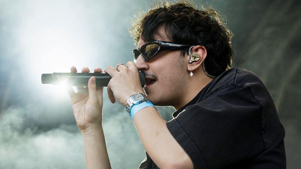 Artemas on stage, wearing dark glasses and singing into a microphone, surrounded by dry ice