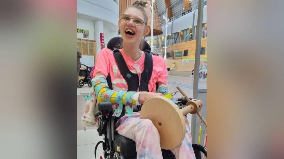 A picture of Taylor Crowe in her wheelchair, smiling 