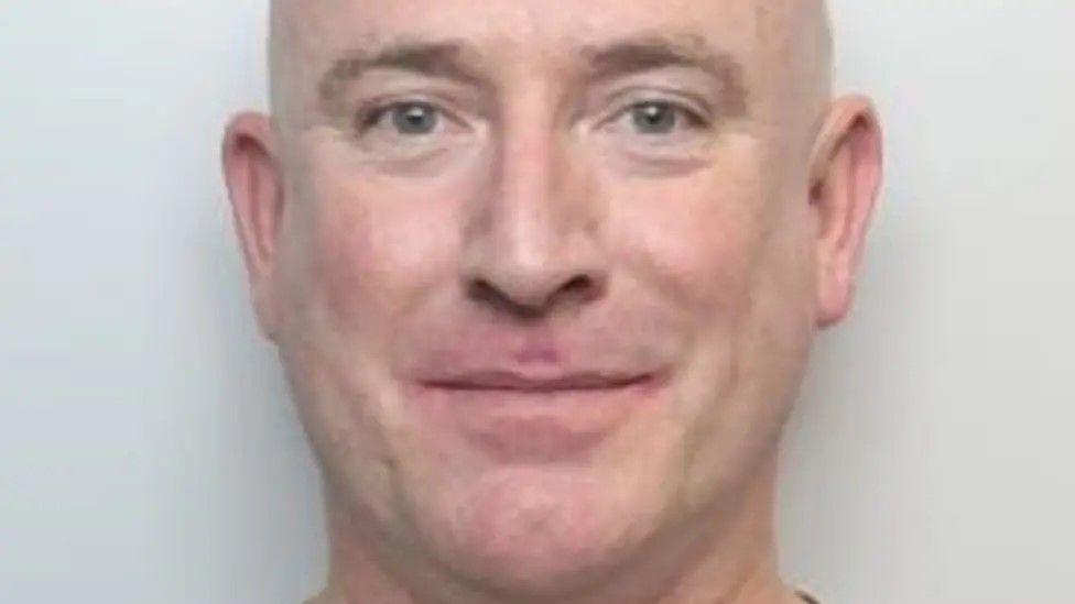 A close-up crop of Martin Underwood's mugshot. He is a bald man. He is smiling without teeth.