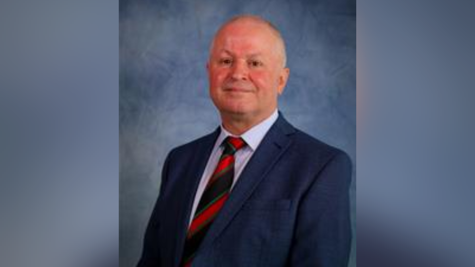 Caerphilly council leader Sean Morgan, wearing a blue suit and red and blue tie, smiling towards the camera