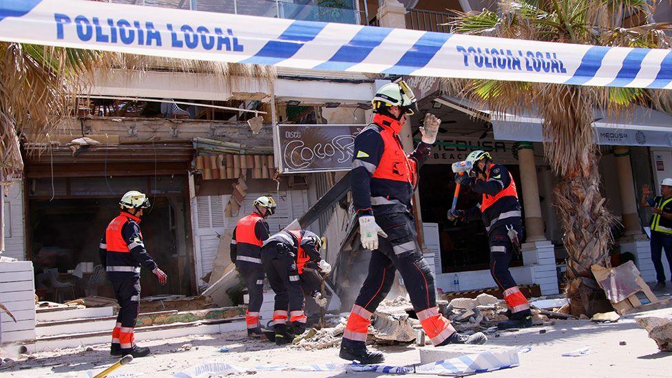 Firefighters gesture outside the site of the collapsed building in Palma on 24 May