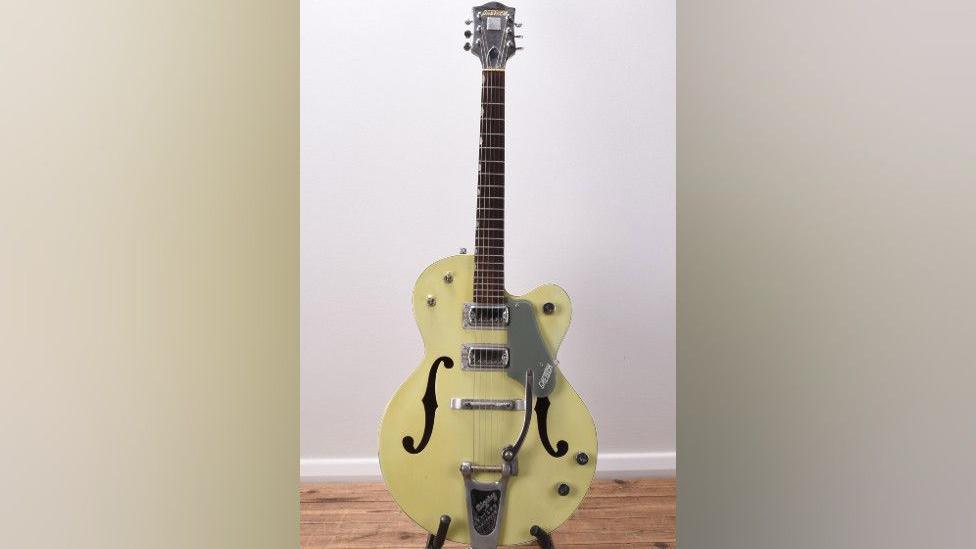 A light green guitar on a stand. It has a Gretsch logo on it.