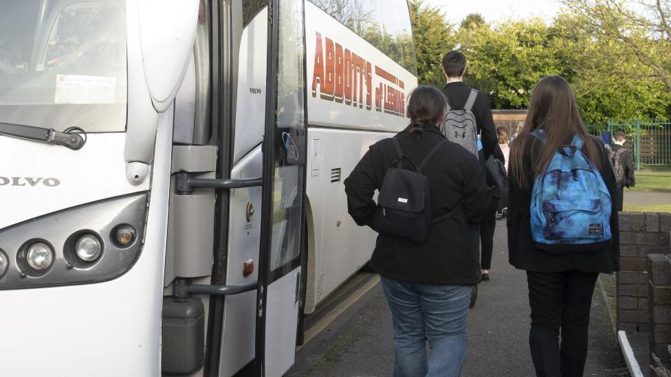 The backs of three children walking off a white school bus