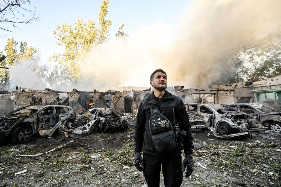 A man is pictured against the background of cars destroyed as a result of Russian shelling