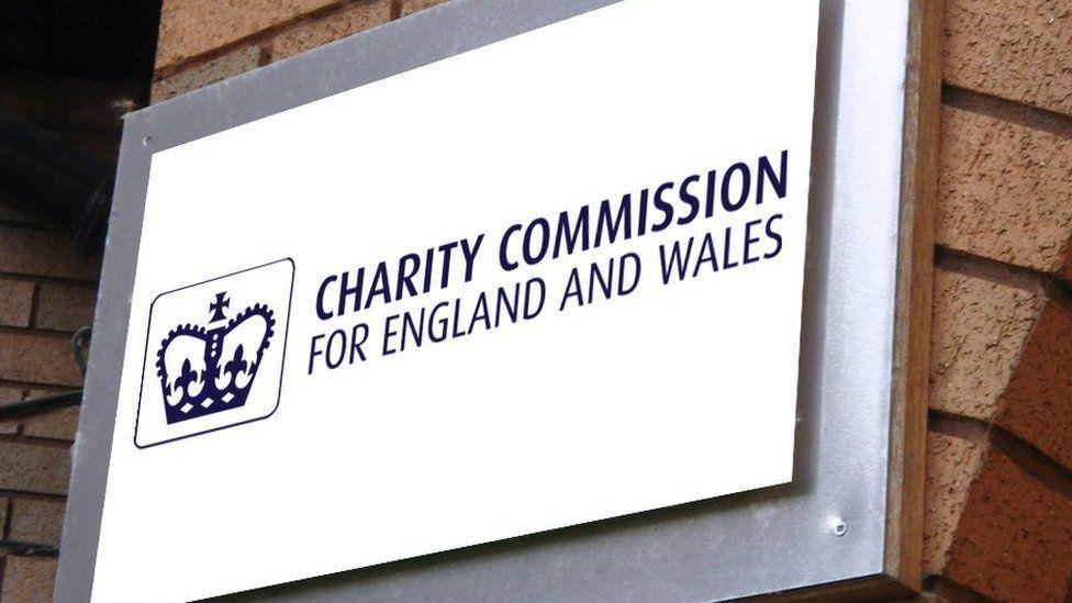 Blue and white sign showing charity commission building. The sign has a crown and is which hung on a brick pillar.