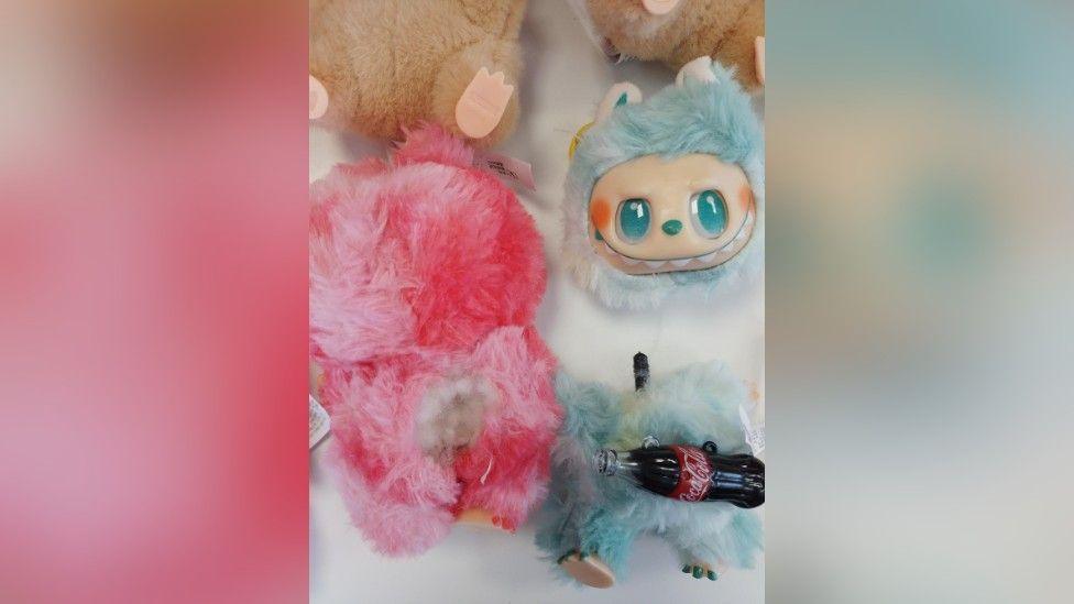 Two of the seized dolls, one pink and one blue, the pink one has a burst seam revealing stuffing and the blue one's head has come off