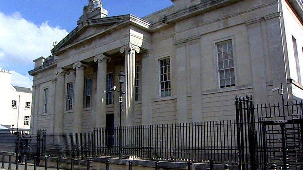 The front of Londonderry Magistrates' Court, The building's four pillars are seen behind a black security railing
