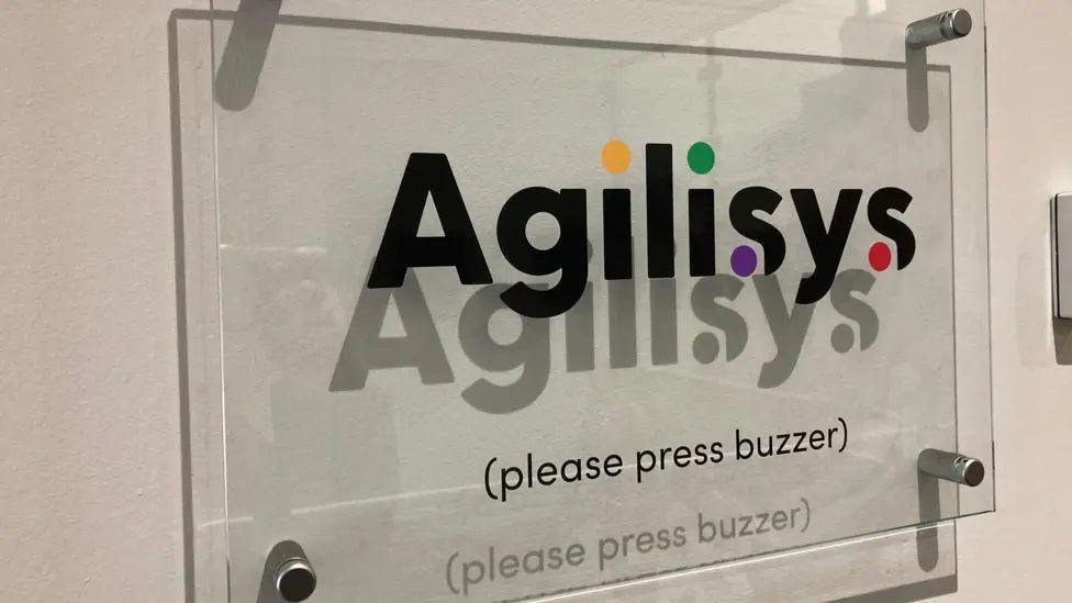 A glass sign mounted on a wall which reads Agilisys (please press buzzer).