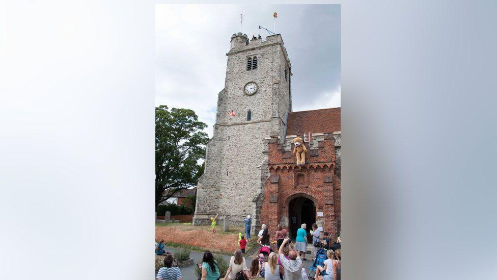 People gathered round the church tower watching as teddy bears are parachuted off it